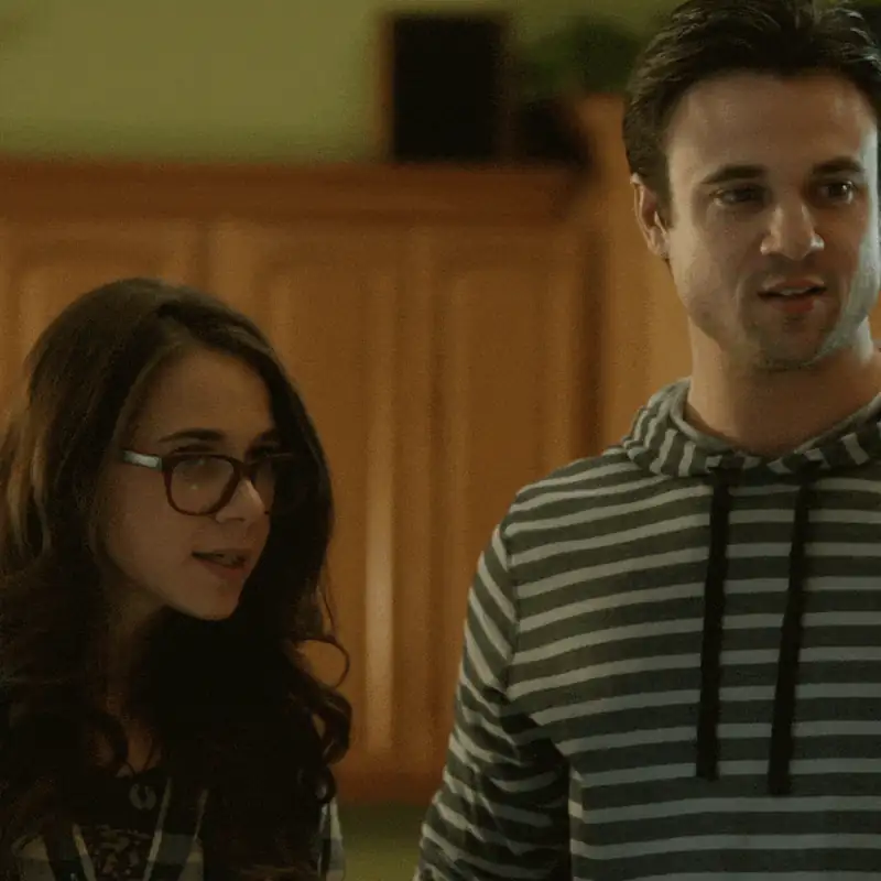 Two young adults engaged in conversation in a cozy indoor setting, both wearing casual striped clothing.