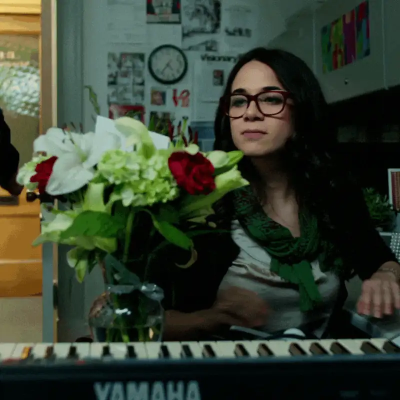 Woman with curly hair and glasses at a keyboard, flowers in a vase, artistic workspace background.
