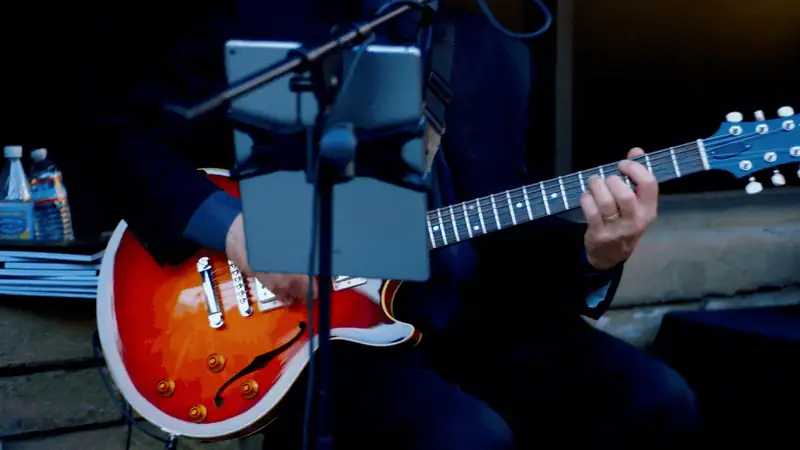 Musician playing an electric guitar with an iPad holder in a performance setting.