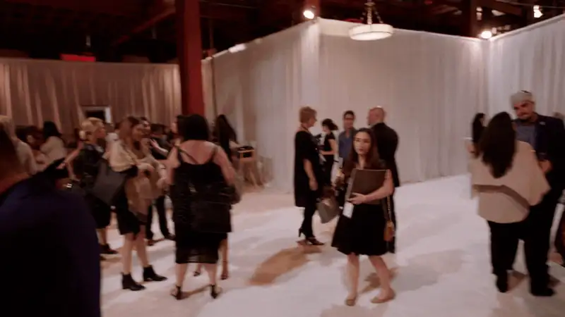 A lively event scene with people networking in a spacious venue adorned with white drapes.