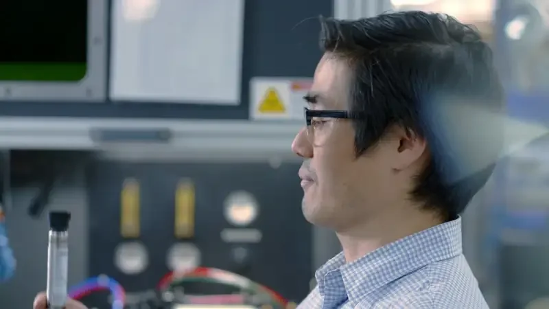 A researcher in glasses holding a pressure instrument in a lab setting.