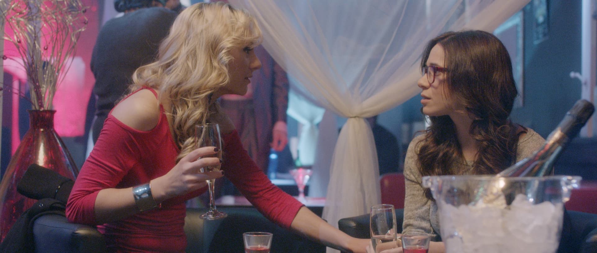 Two women engaged in conversation at a vibrant bar, holding drinks and enjoying their night out.