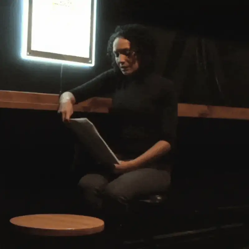 Woman reading from a script in a dimly lit space, focused on her performance.