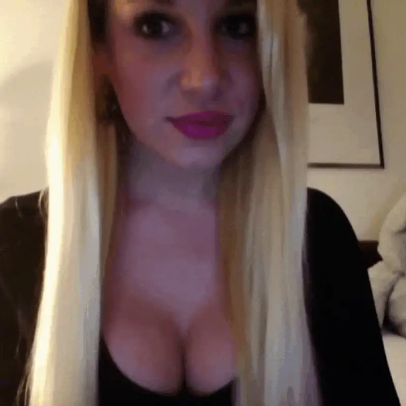 Portrait of a woman with long blonde hair and pink lipstick, dressed in black, in a cozy indoor setting.