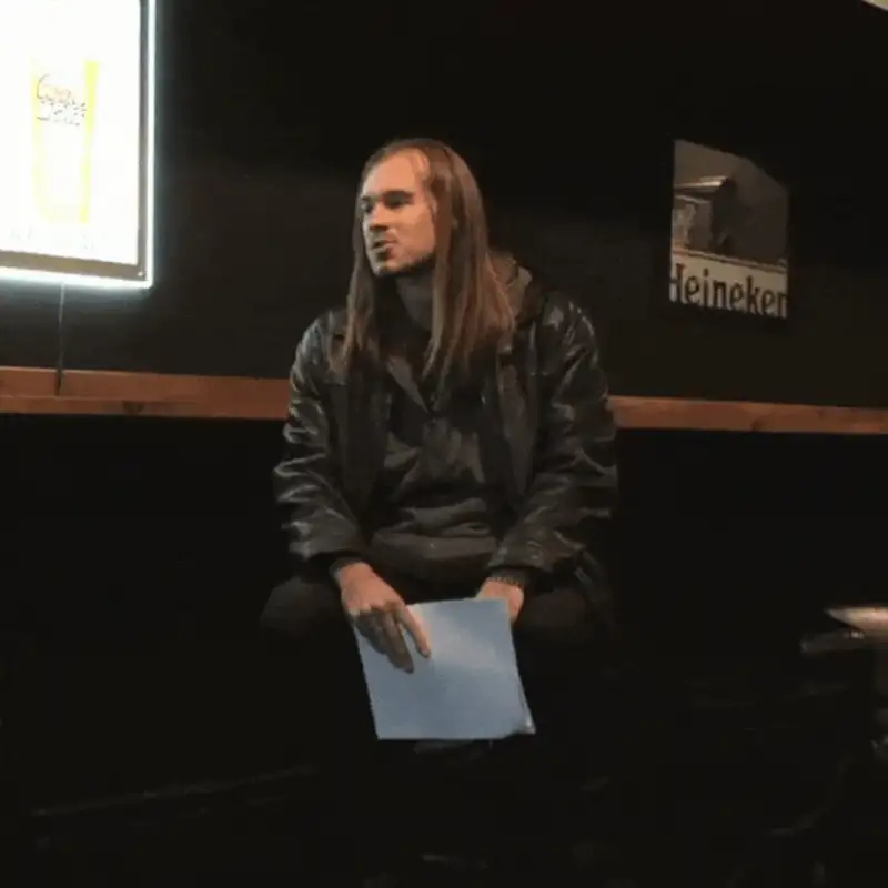 Person sitting with paper in hand, illuminated backdrop featuring beer advertisement.