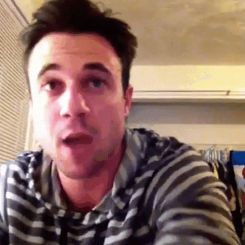 Man in striped hoodie speaking passionately during a video call in a casual setting.