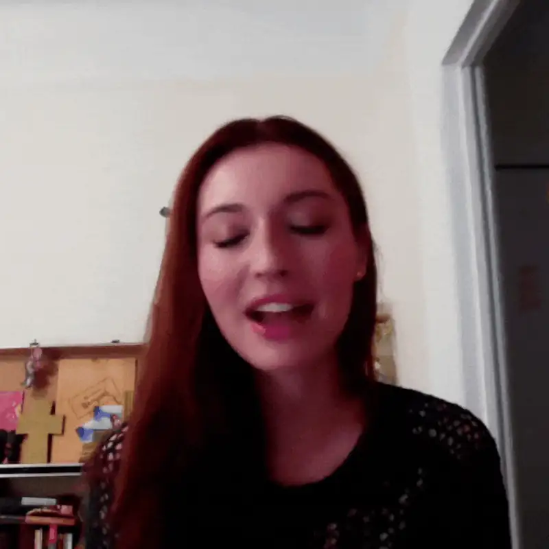 Woman with long brown hair smiling while speaking, with a creative workspace in the background.