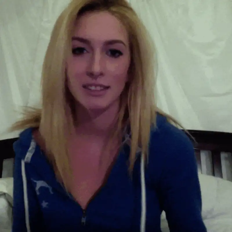 Smiling person with long blonde hair wearing a blue hoodie, sitting against a white background.