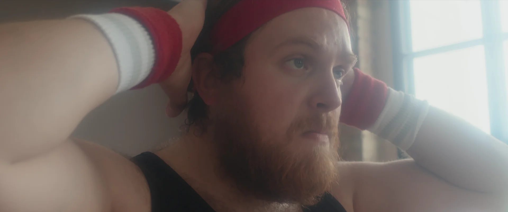 Man adjusting his headband in a bright room, wearing workout gear with red and white wristbands.