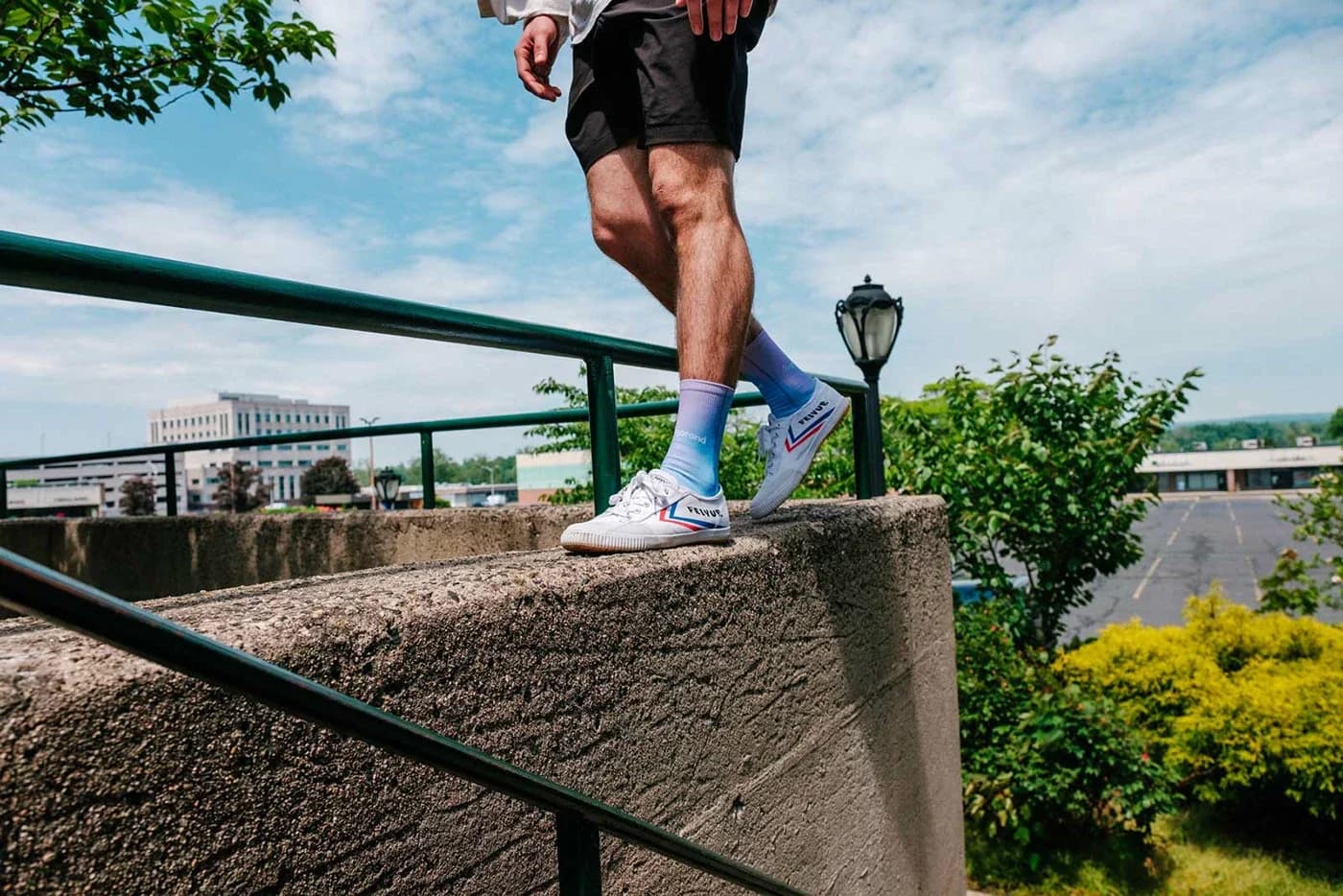 Person walking down a railing onto a concrete ledge wearing white sneakers and blue socks.