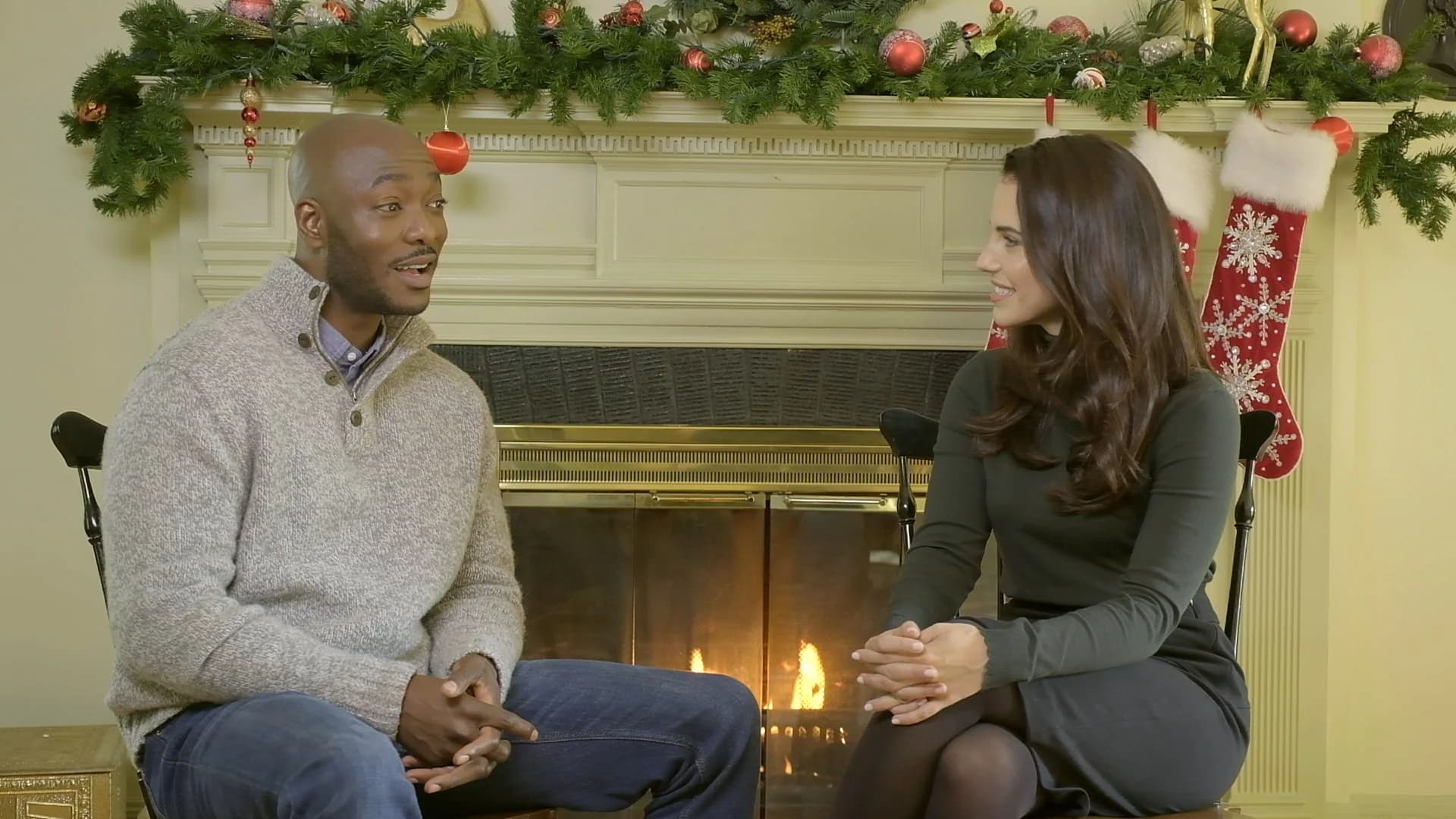 Two people sitting by a decorated fireplace during a holiday gathering.
