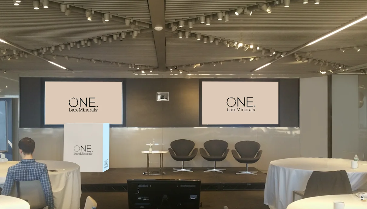 Conference setup with 'ONE. bareMinerals' branding and chairs arranged for a presentation.