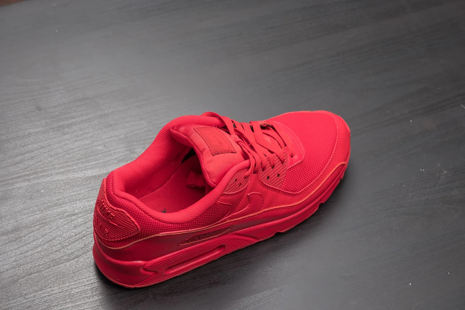 Red Nike Air Max sneaker displayed on a dark wooden surface.