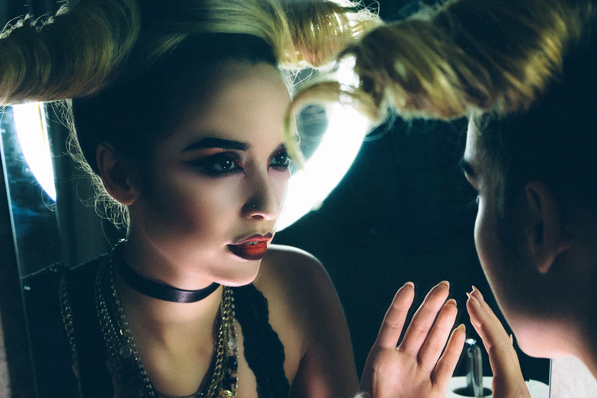 Close-up of stylish woman with bold makeup and unique hairstyle, gazing into a mirror, capturing a dramatic moment.