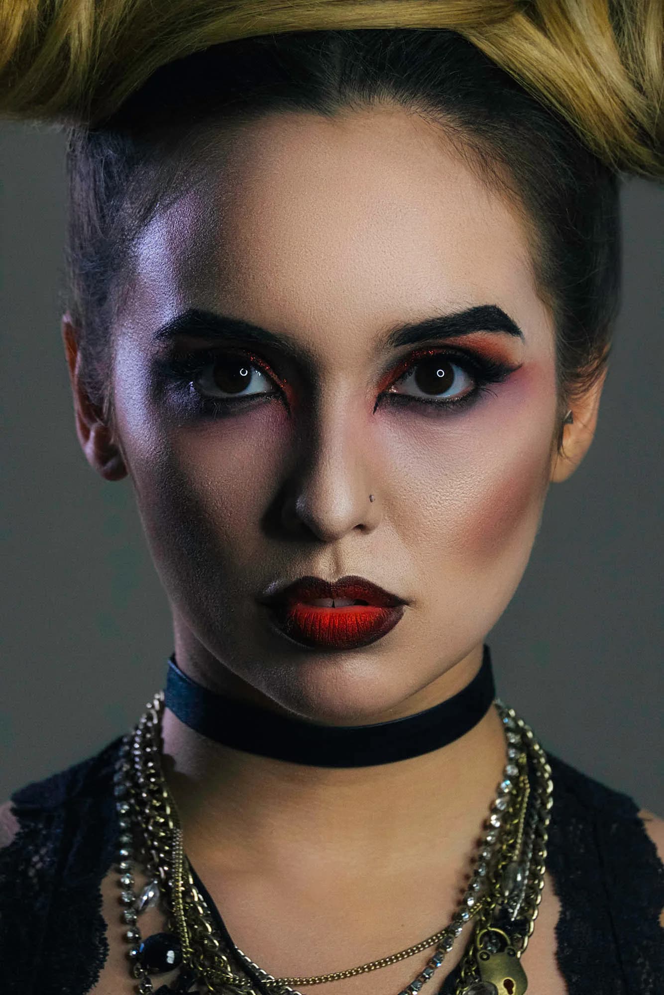 Close-up of a model with dramatic makeup, bold red lips, and layered necklaces, showcasing bold beauty aesthetics.