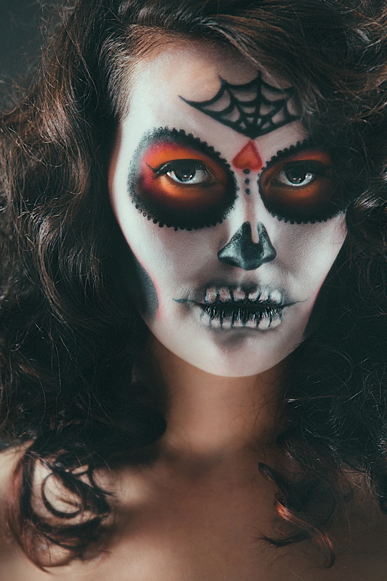 Close-up of a woman with artistic Day of the Dead skull makeup and dark, wavy hair.